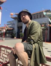 Rapper jason chu sitting along a fence with China Town in the background.